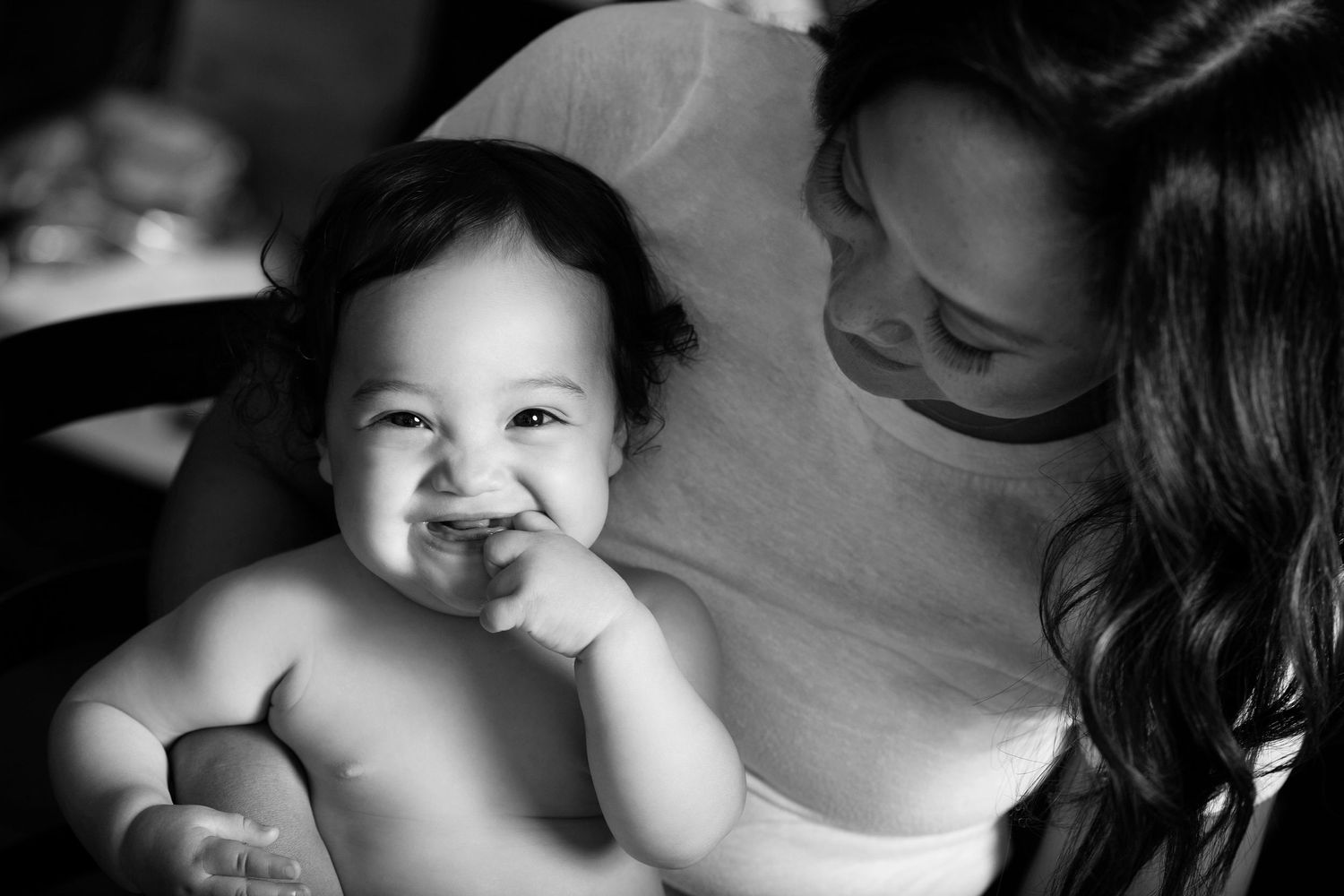 Black and white candid photo of smiling baby with caregiver.