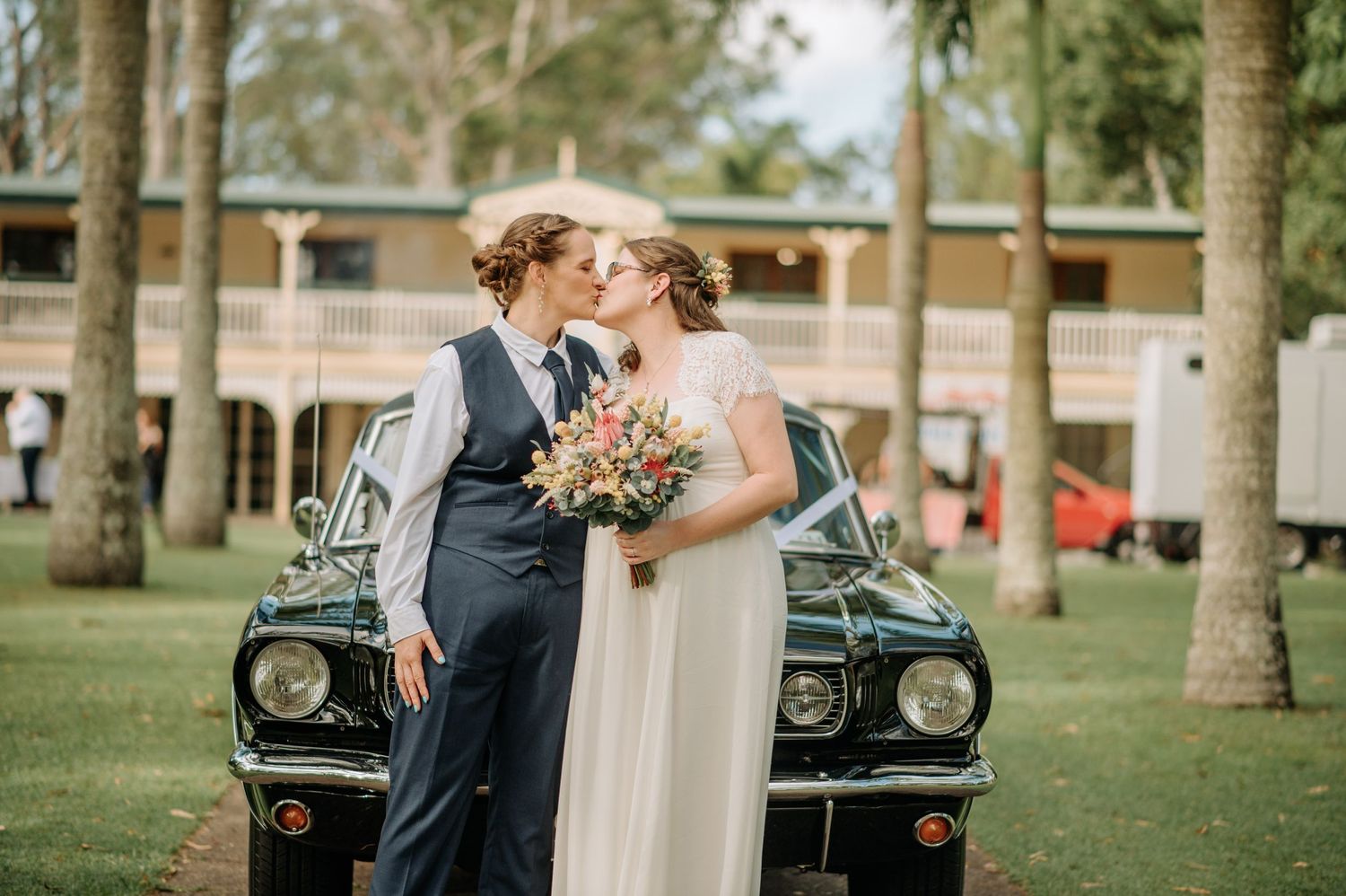 Couple shares romantic moment in front of vintage car surrounded by palm trees.