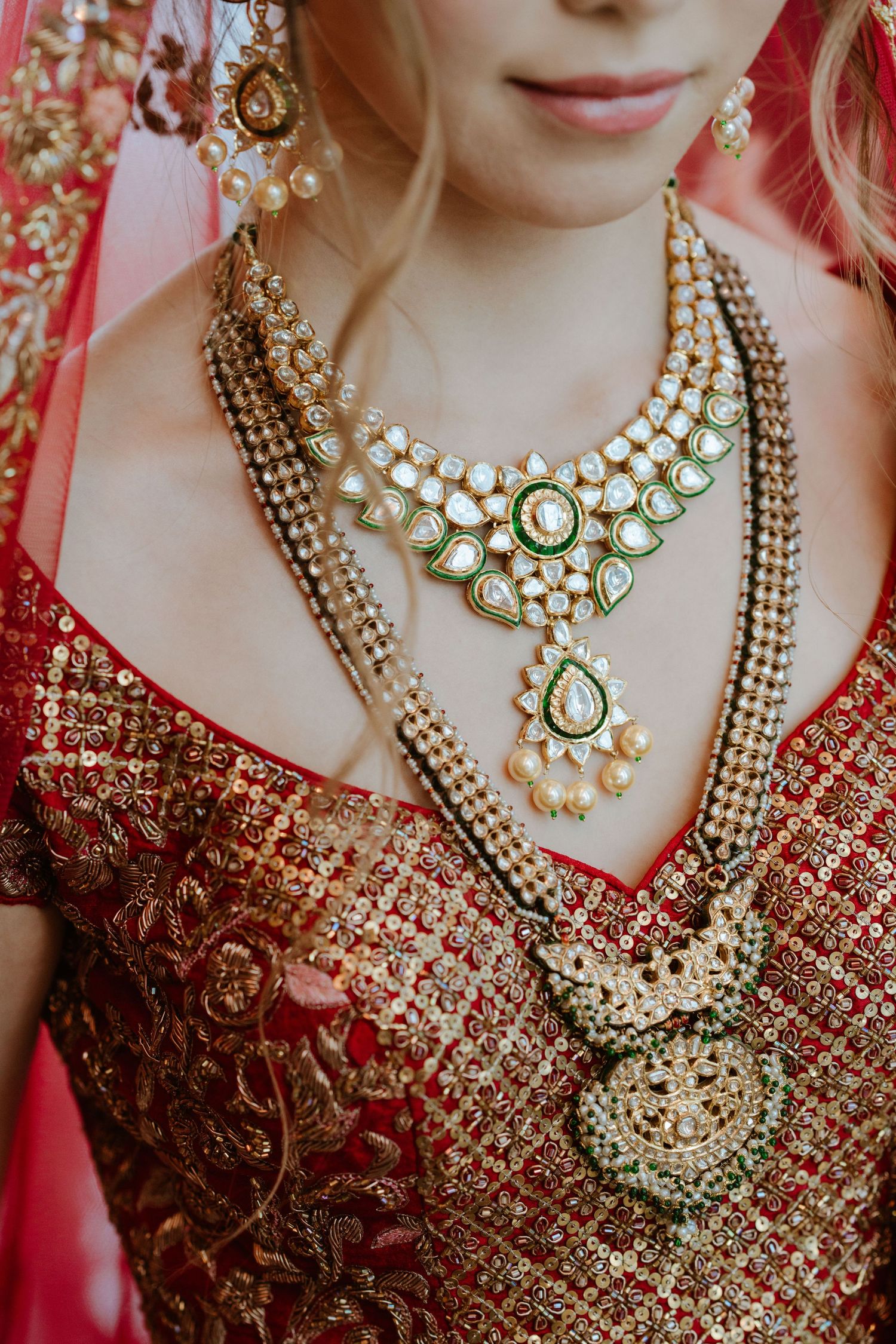 Elegant kundan necklace with emerald and pearl details against a red embroidered wedding dress.