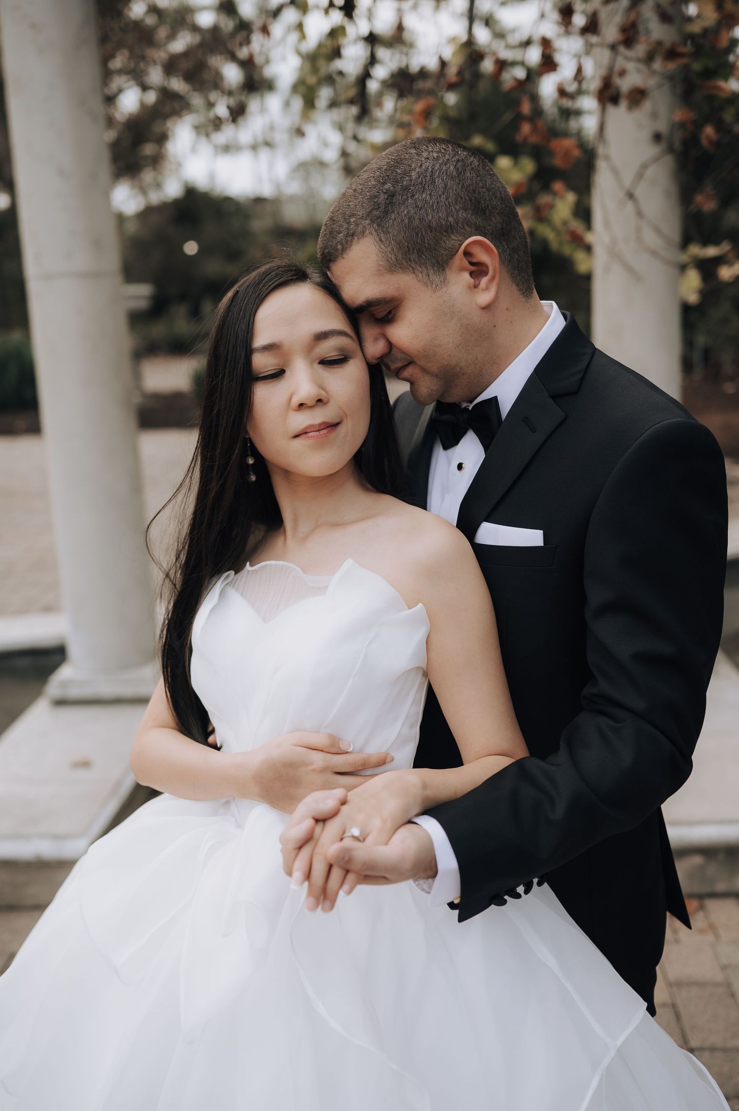 A tender moment between newlyweds in formal attire against a classic column backdrop.