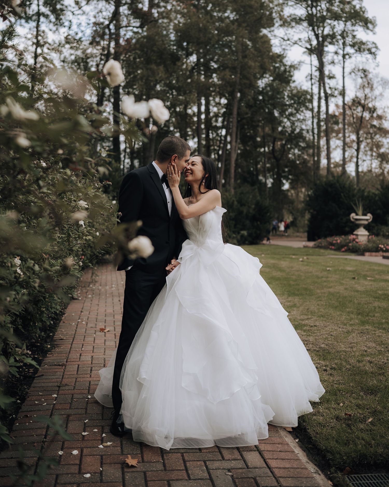 A wedding couple shares a romantic moment on a garden pathway with floating white balloons.