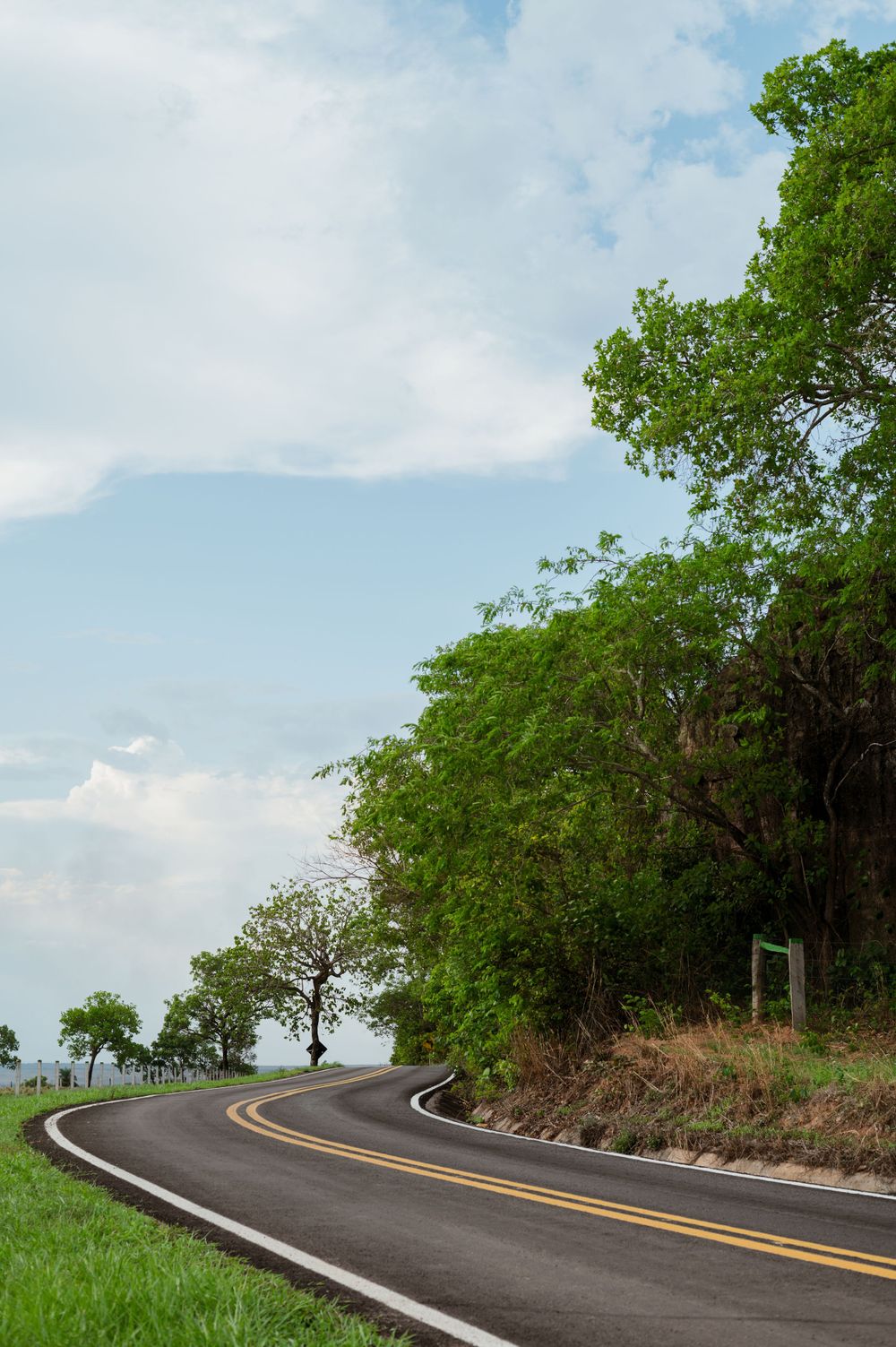 Winding rural road curves through lush green landscape under blue sky.