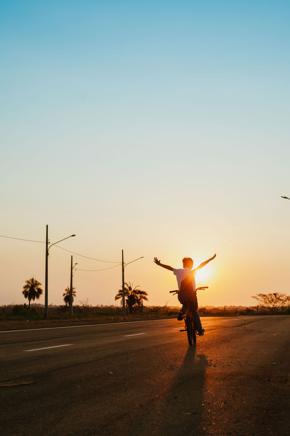 Cyclist silhouetted against orange sunset sky with arms raised in triumph.