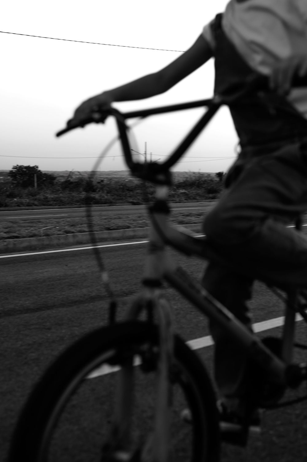 Close-up black and white shot of hands gripping bicycle handlebars on open road.