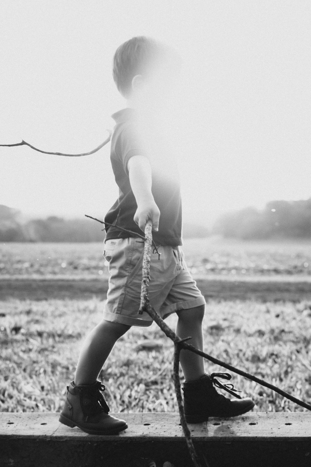 High-key black and white silhouette of child walking with stick outdoors.
