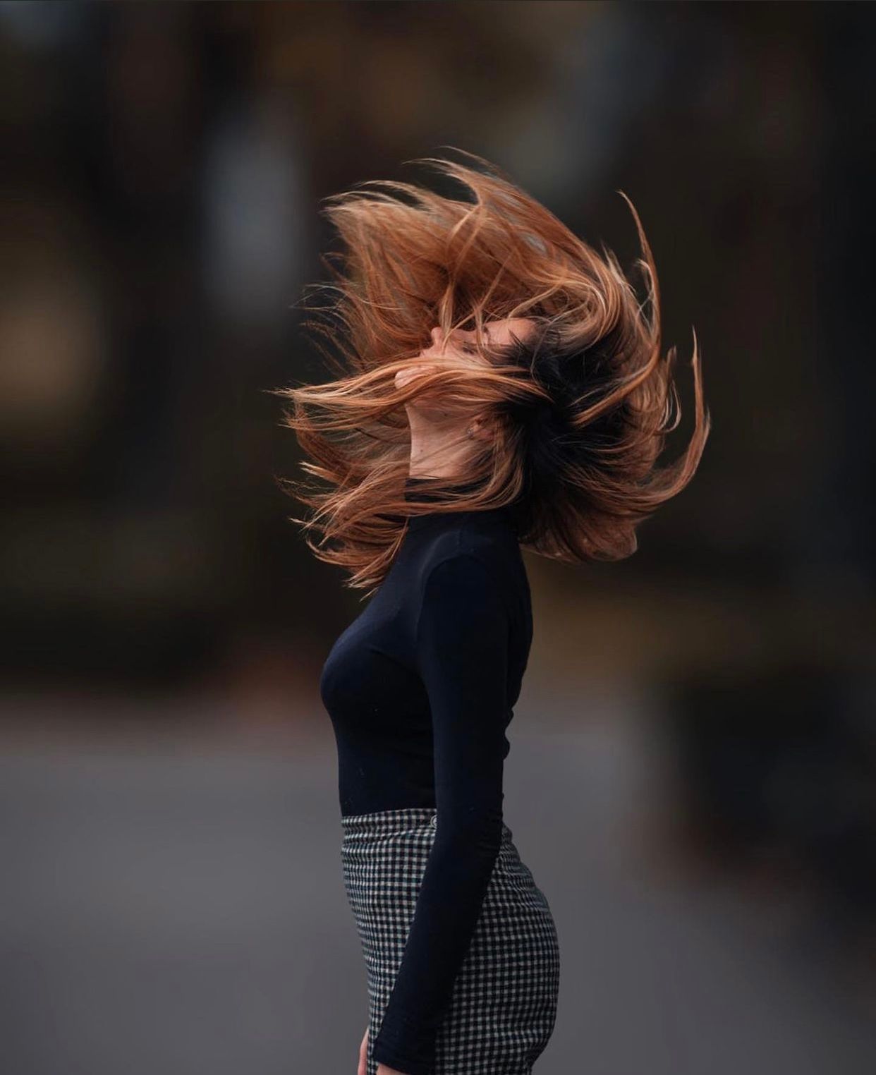 Person with flowing red hair in motion against dark background.