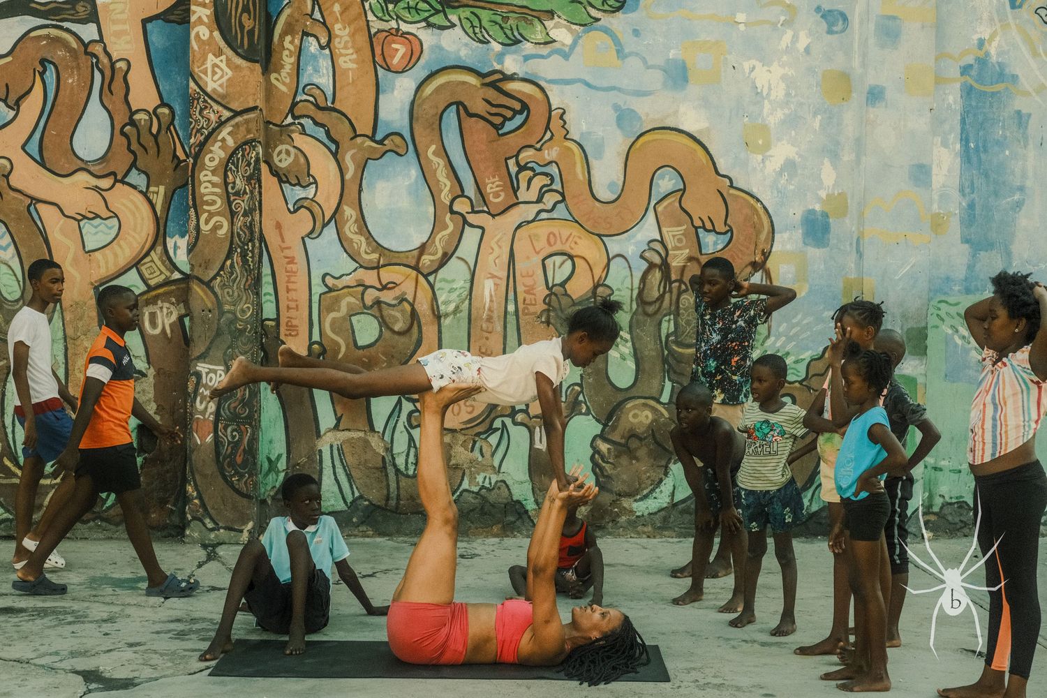 A group practices acrobatic moves against a colorful street art mural.