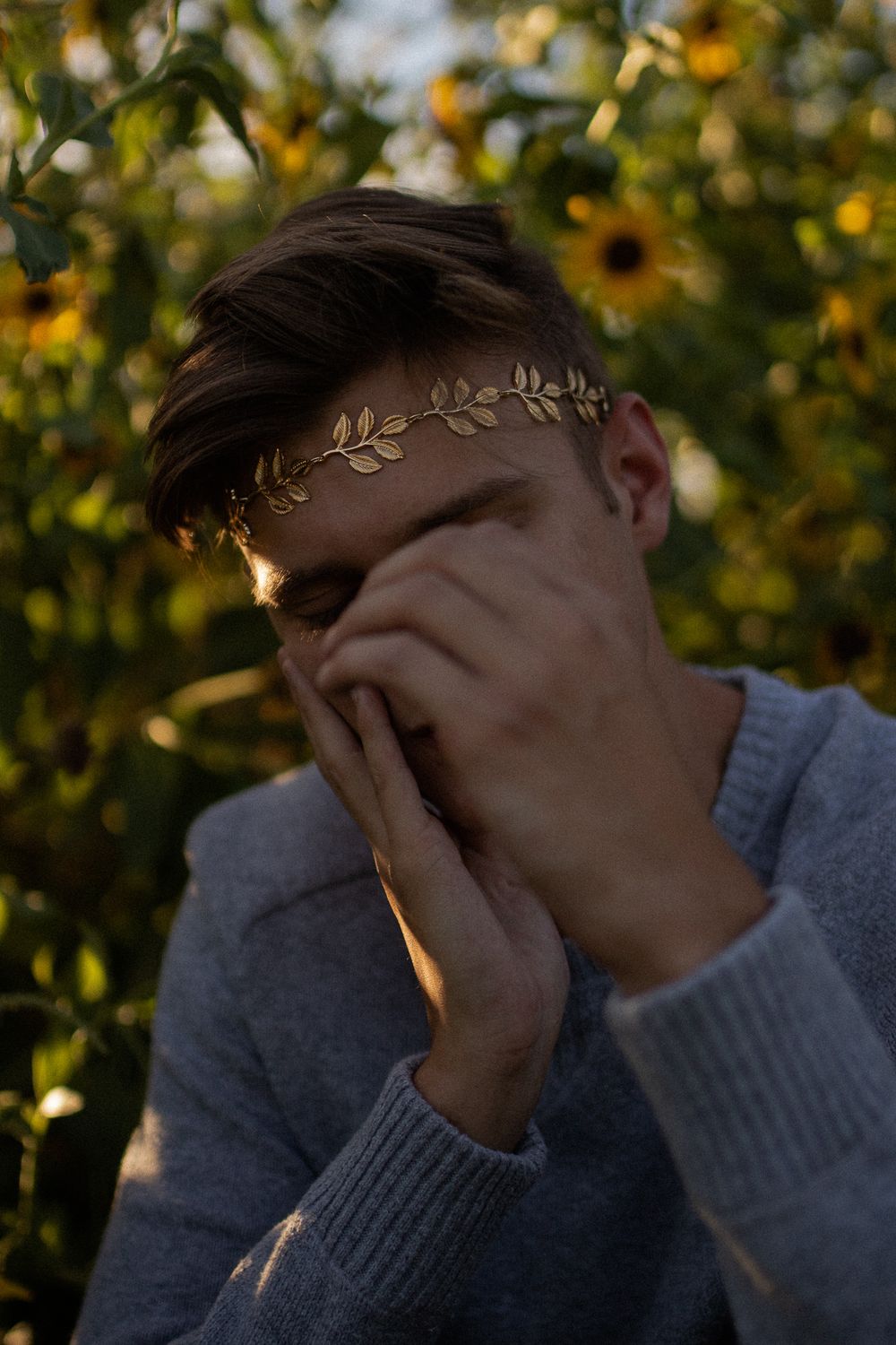 Emotional portrait with decorative leaf crown against sunflower garden at sunset.