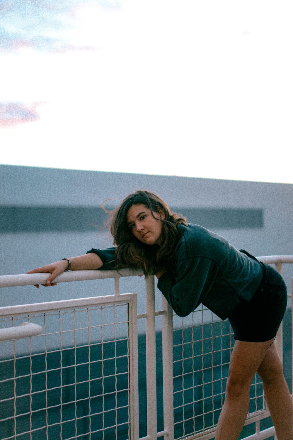 Casual portrait leaning on railing during sunset with urban backdrop.