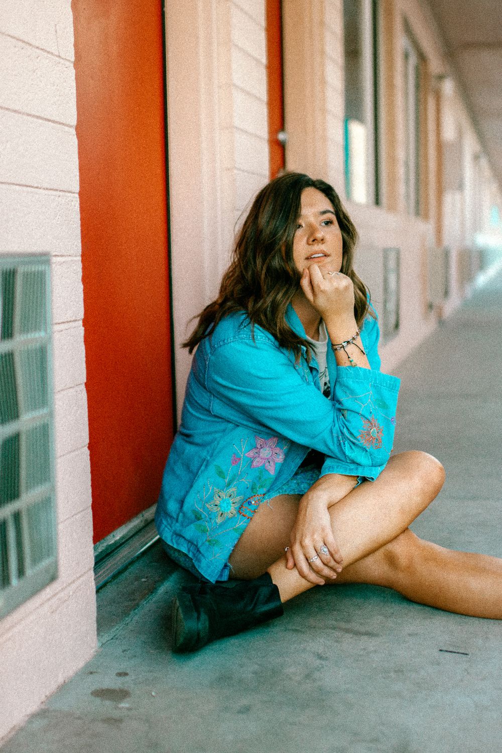 Candid portrait in embroidered turquoise jacket sitting against coral-colored wall.