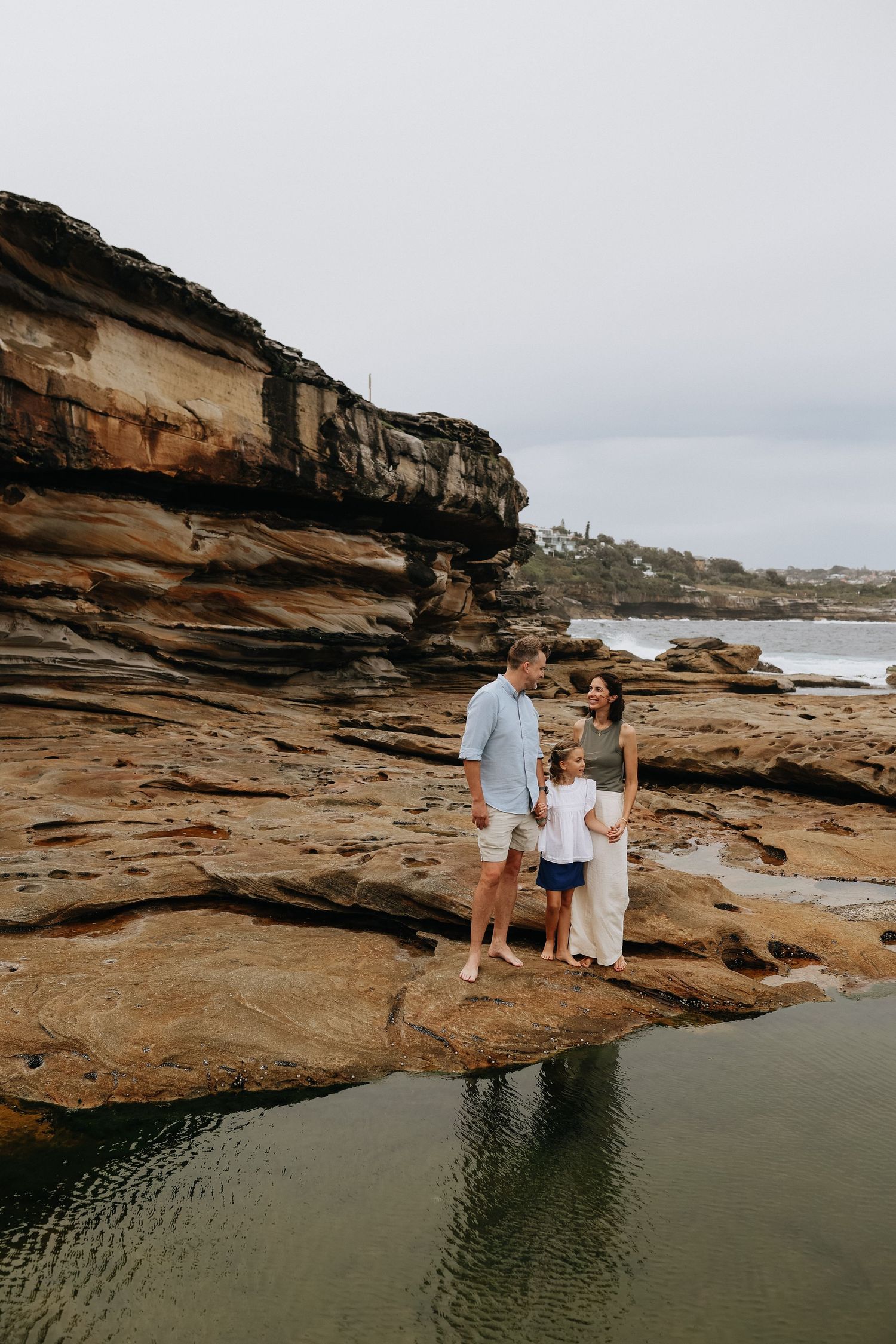 Family of three standing on rocky coastal cliffs with ocean views in an outdoor portrait session.
