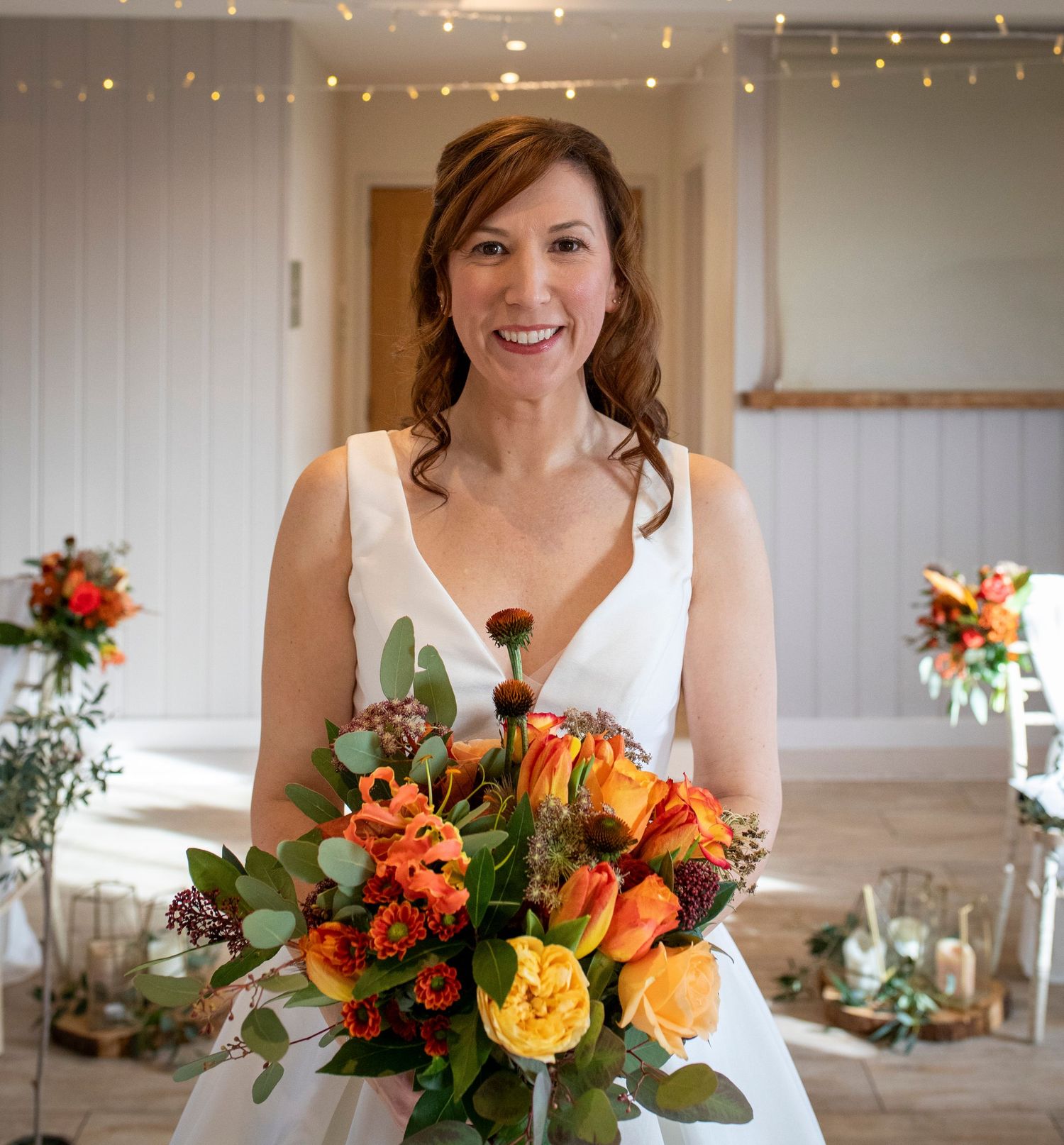 Bride holding vibrant orange and yellow fall wedding bouquet in white reception venue.