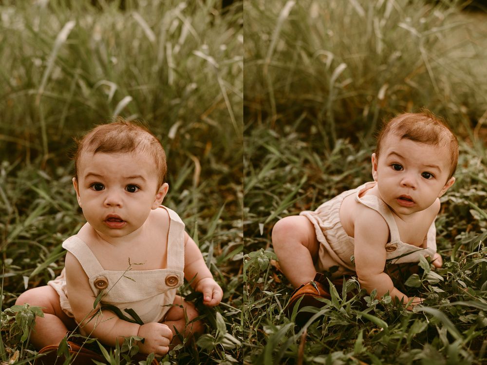 Two babies wearing tan overalls sitting together in tall green grass during golden hour.