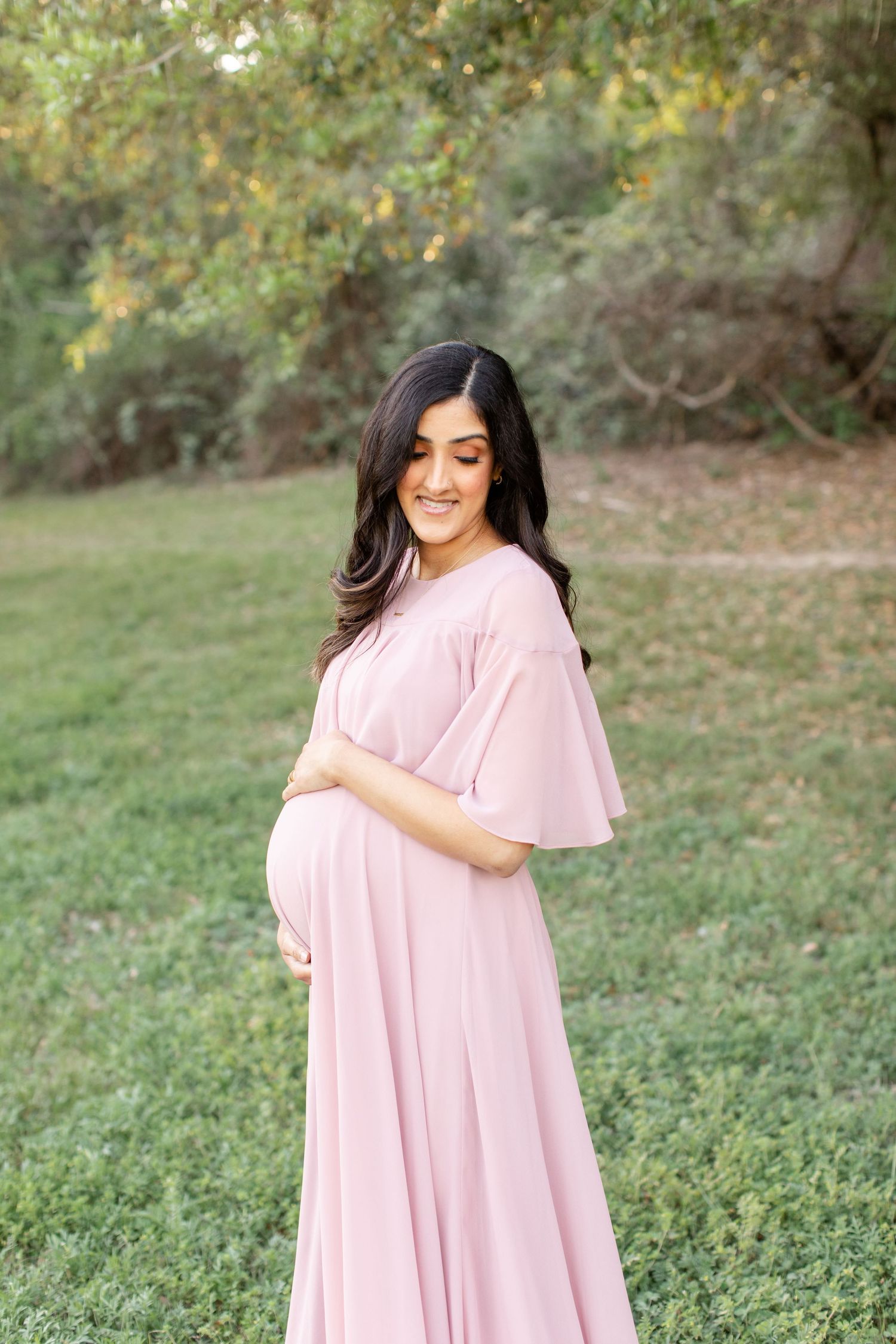 A flowing blush maternity dress captures a joyful moment in a sunlit garden.