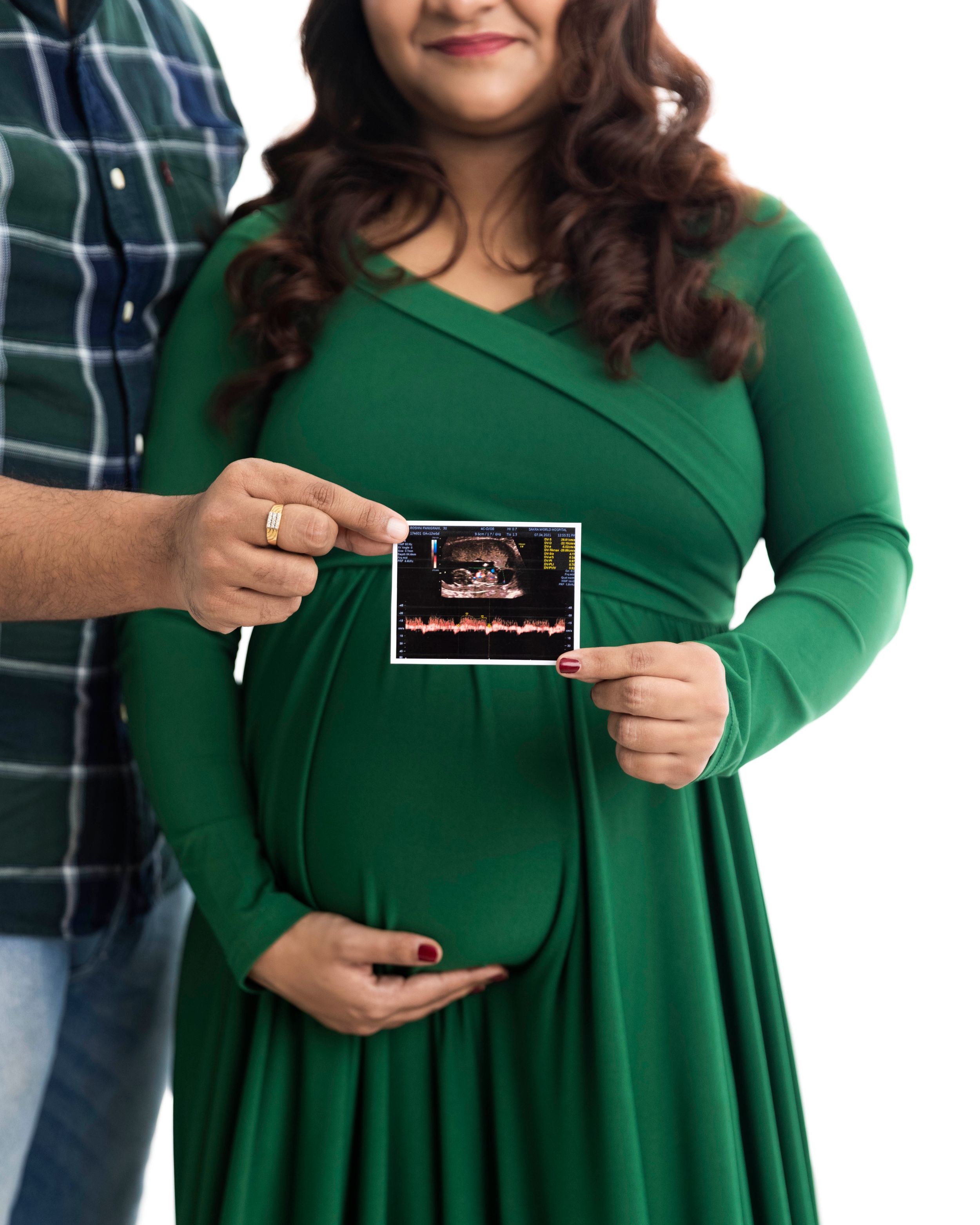 Couple holding ultrasound photo while wearing green dress and plaid shirt.
