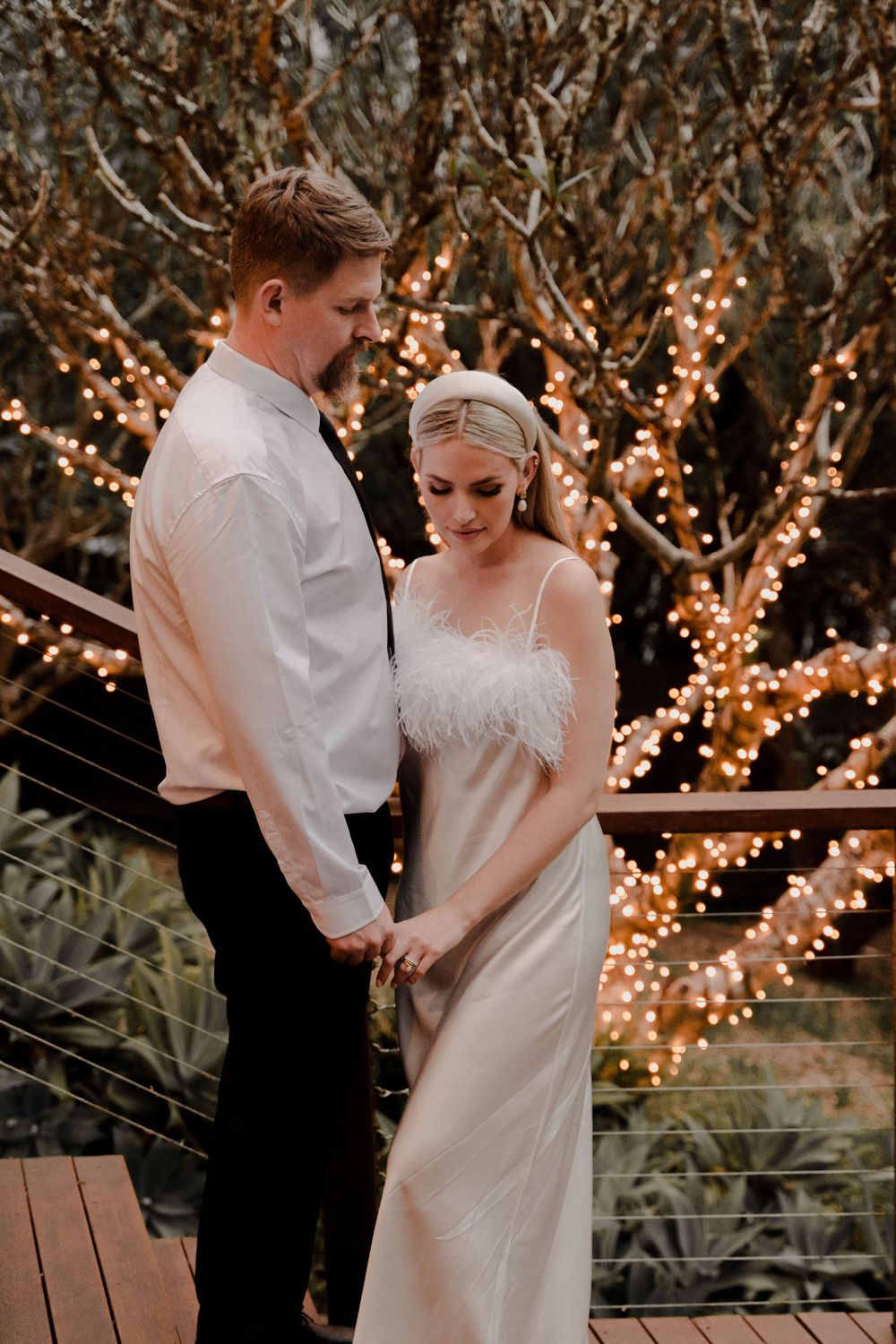 Couple in wedding attire share intimate moment under twinkling garden lights.