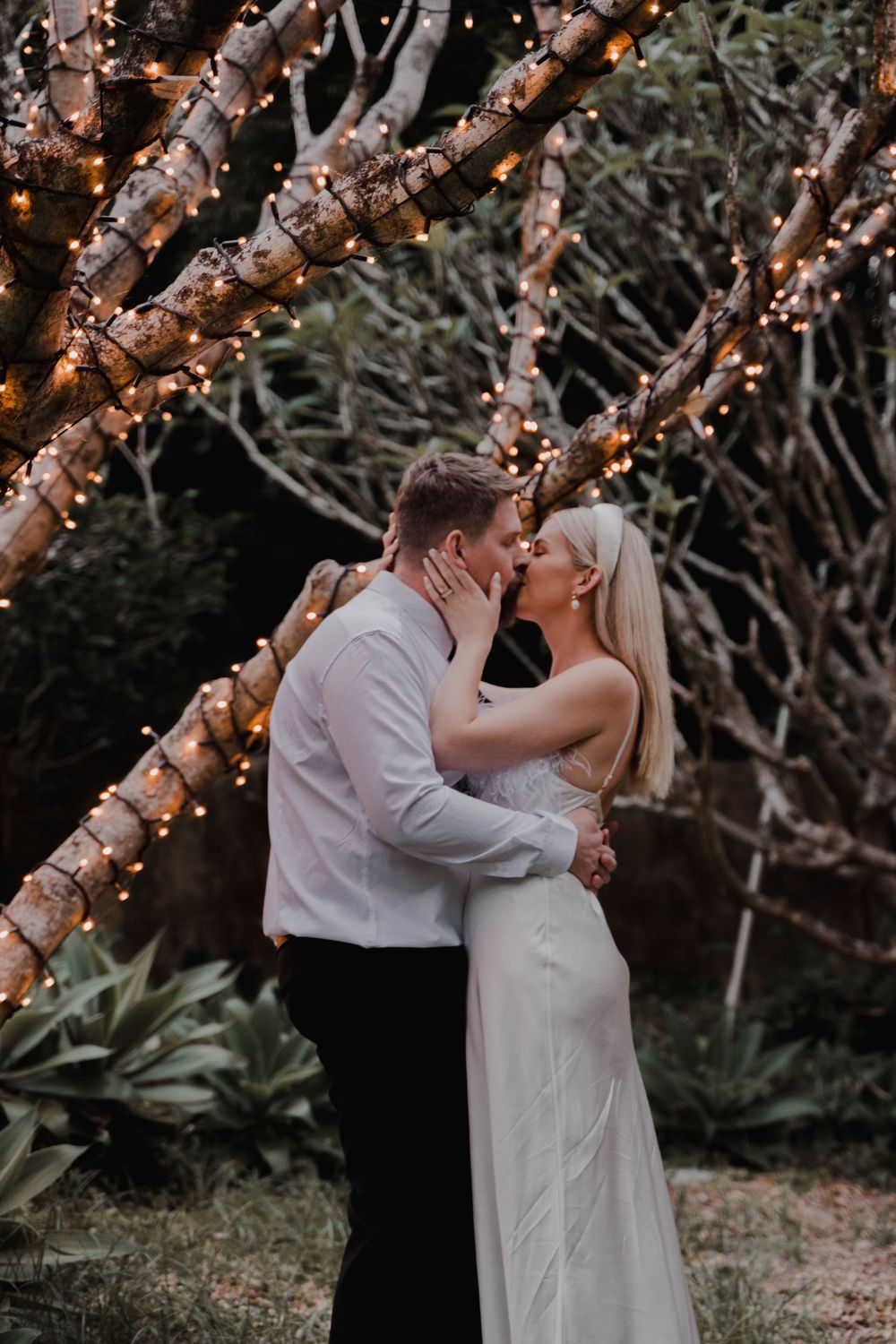 Romantic evening portrait under trees decorated with warm glowing string lights.