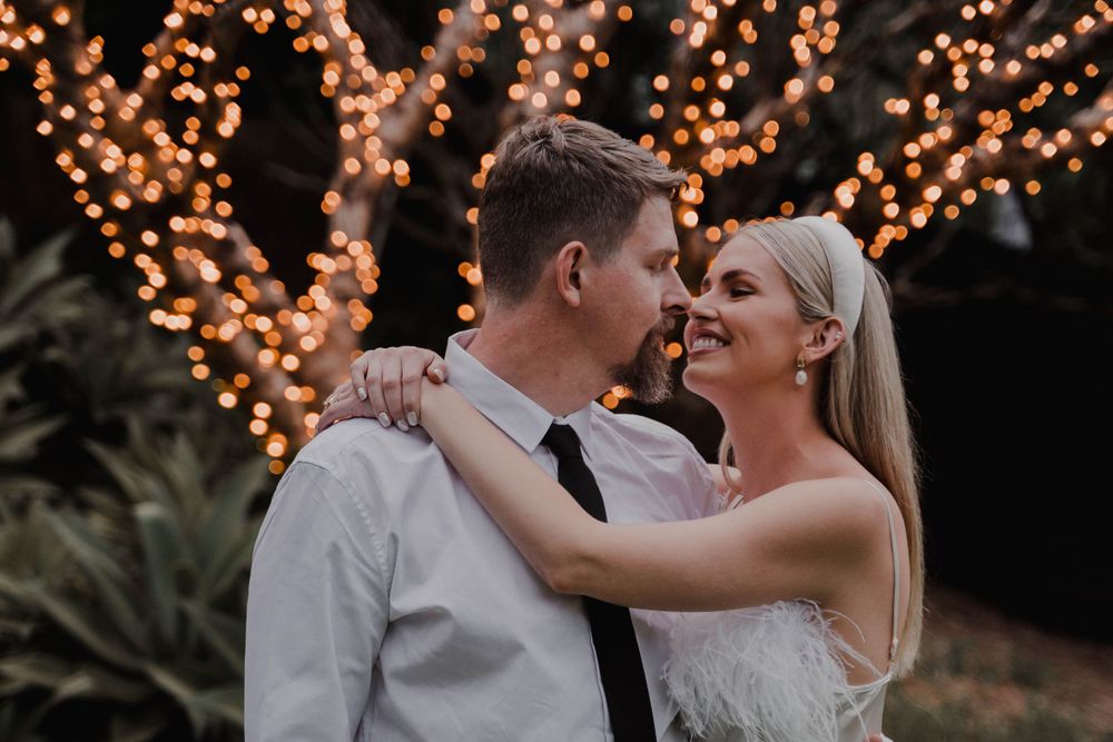 Candid moment of laughter between couple beneath trees illuminated with fairy lights.
