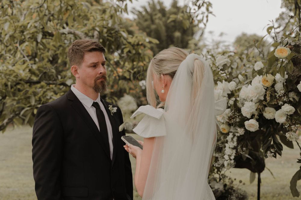 A bride and groom share a moment under white floral arrangements in a garden setting.
