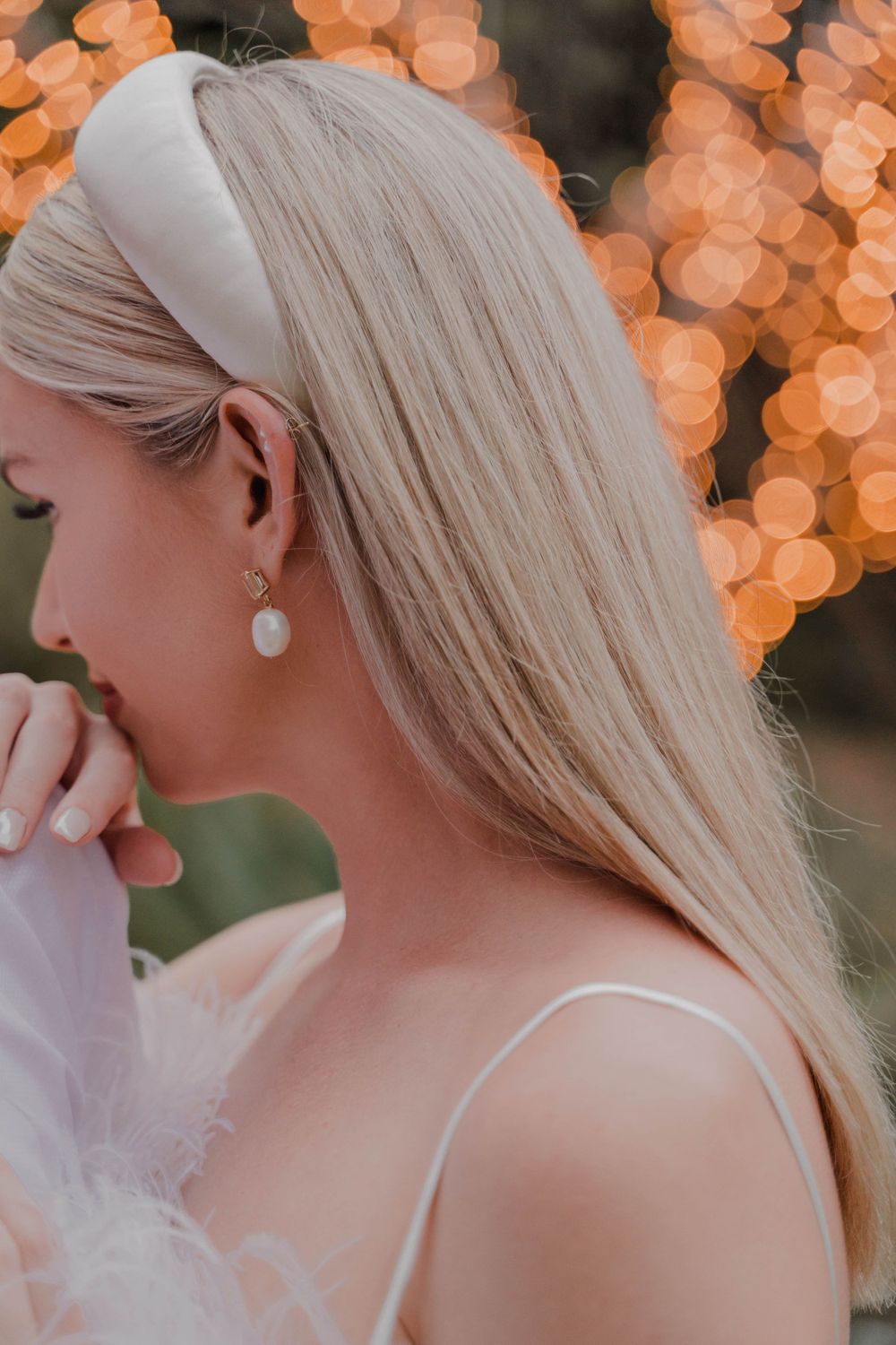Elegant side profile with platinum blonde hair wearing a white headband against warm bokeh lights.