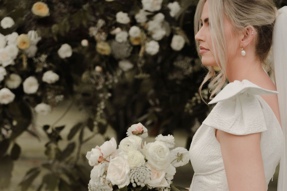 Bride holding elegant white rose bouquet against backdrop of flowering bushes.