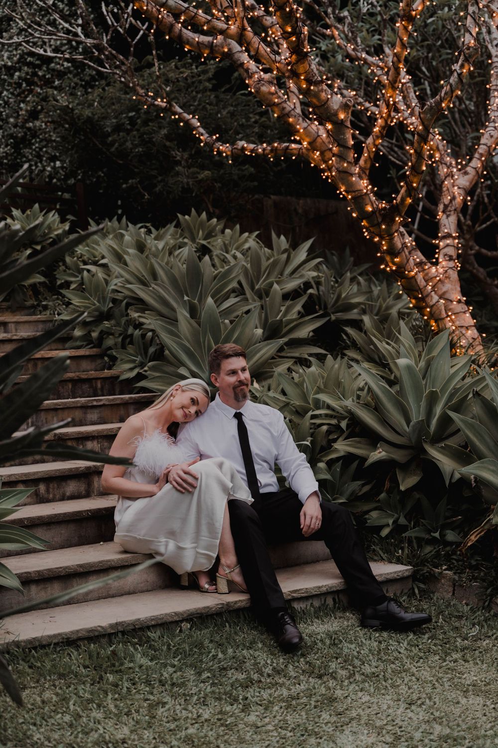 Couple resting on garden steps surrounded by agave plants and illuminated trees.