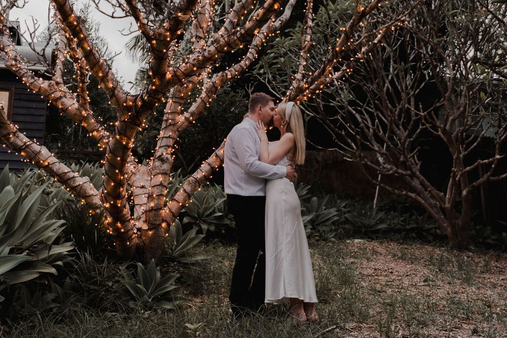 Intimate moment between newlyweds under trees adorned with twinkling fairy lights.