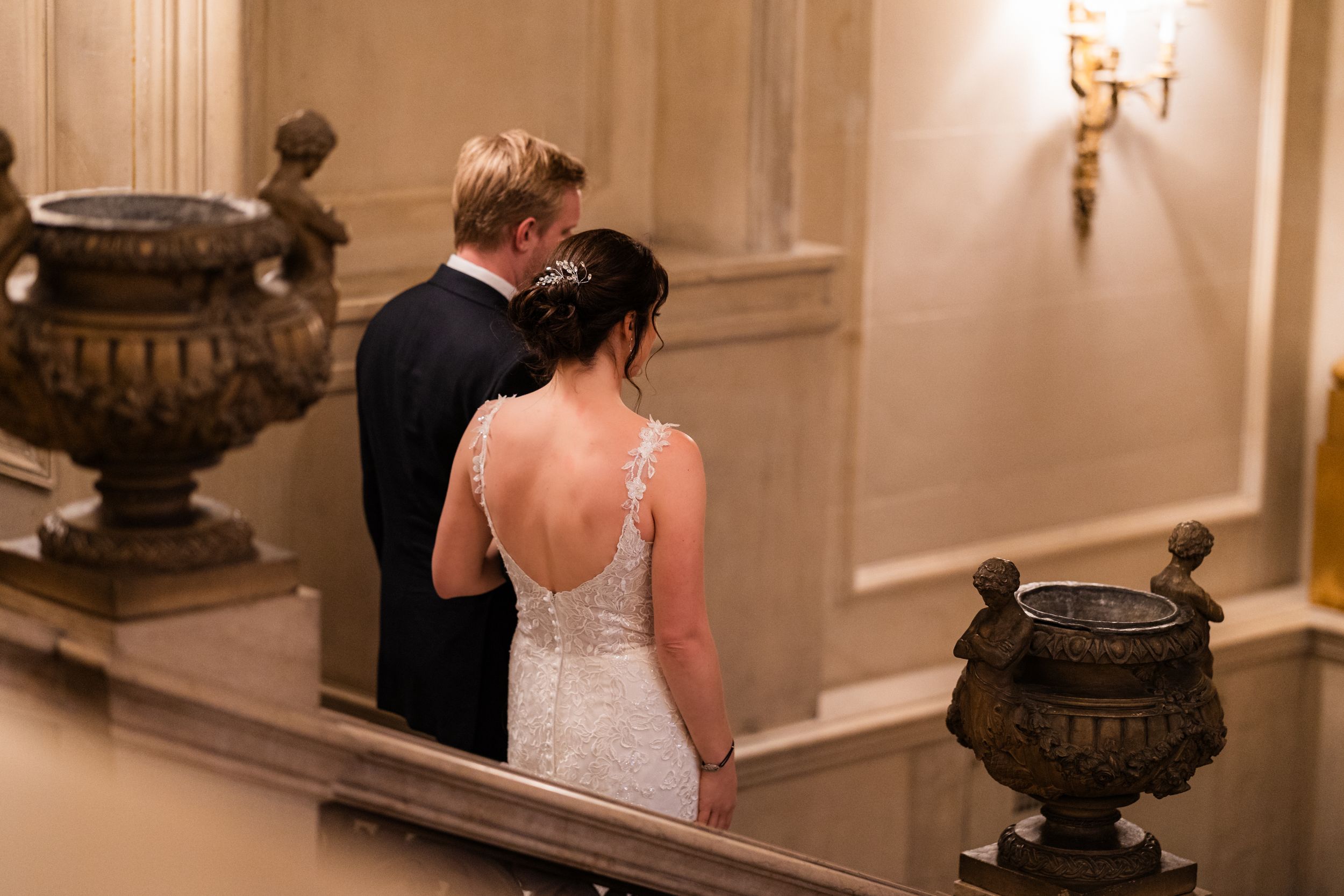 A couple ascending an elegant staircase at Larz Anderson House in Washington, DC with ornate urns and wall sconces.