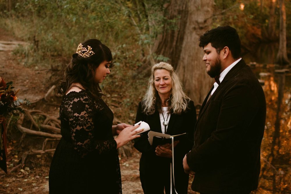 Intimate woodland ceremony with couple in dark formal wear and officiant.
