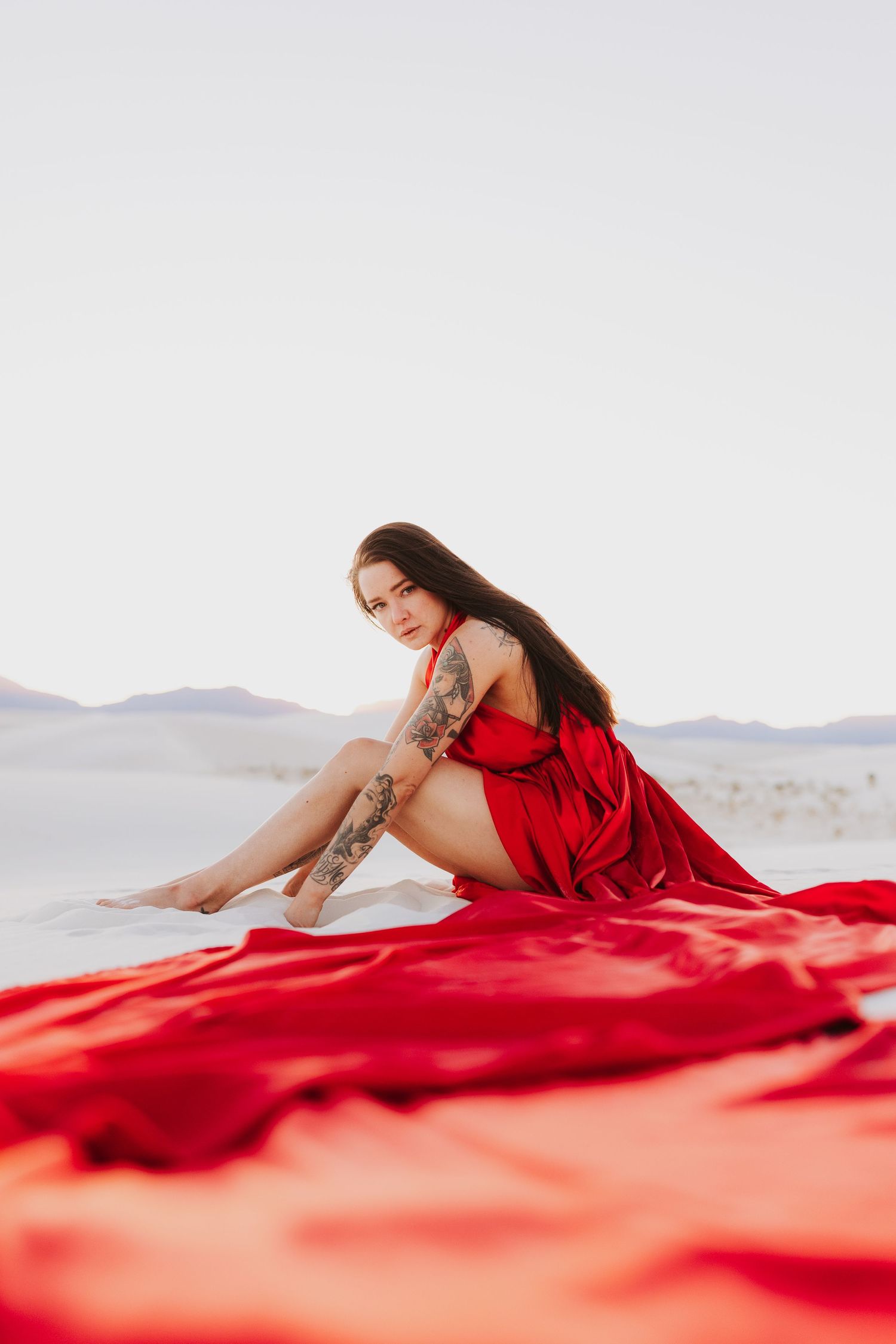 Figure in flowing red dress poses dramatically on white background with mountain silhouette.