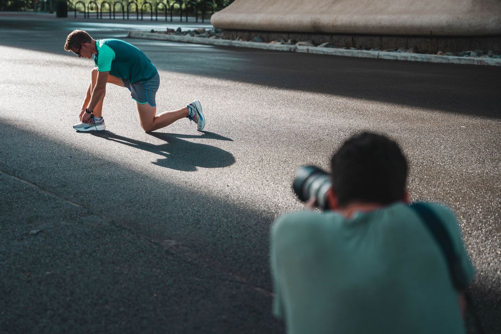 Photographer capturing athletic pose under bridge in dramatic lighting.