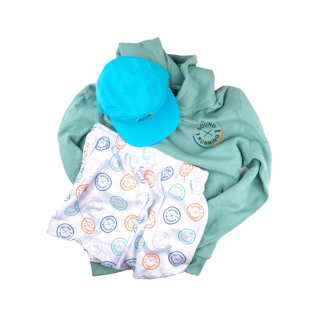 Mint green sweatshirt with matching pom beanie and patterned shorts laid flat on white background.
