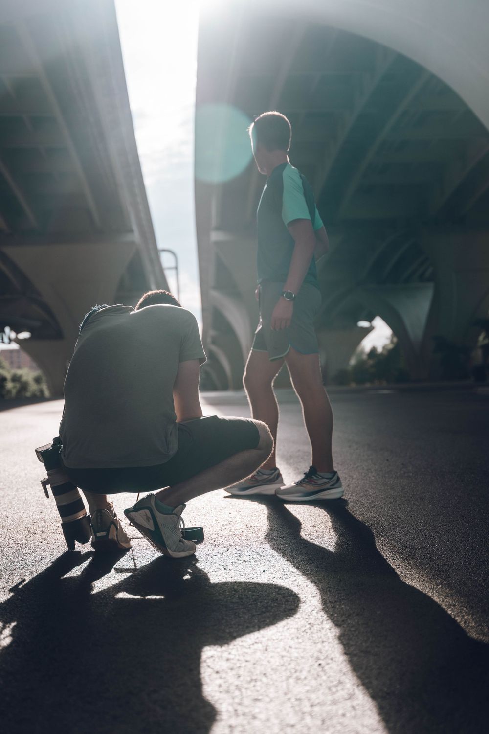 Photographer and subject working on athletic photo shoot under concrete bridge.