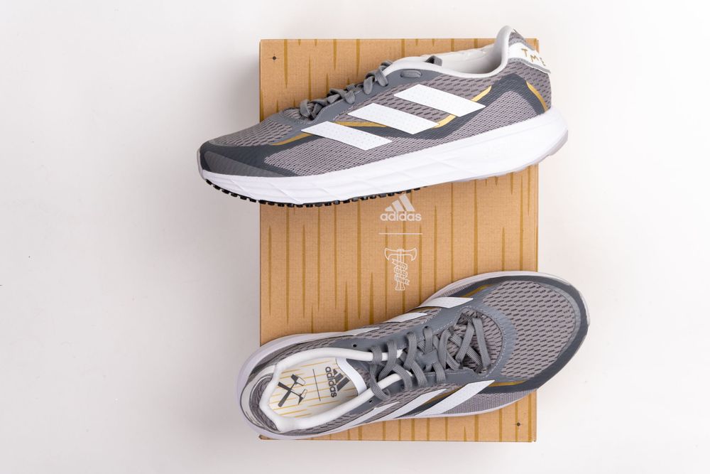 Grey and white Adidas running shoes displayed on wooden surface.
