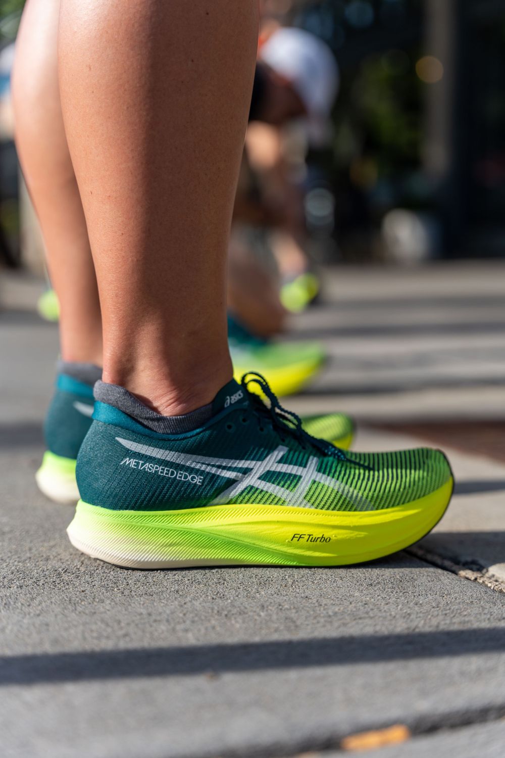 Close-up of green and yellow Asics running shoes on pavement during outdoor activity.