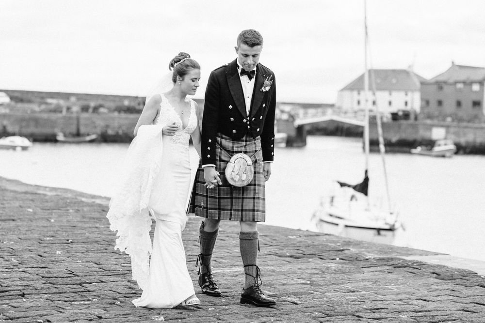 Romantic wedding portraits captured along a seaside harbor with boats in the distance.