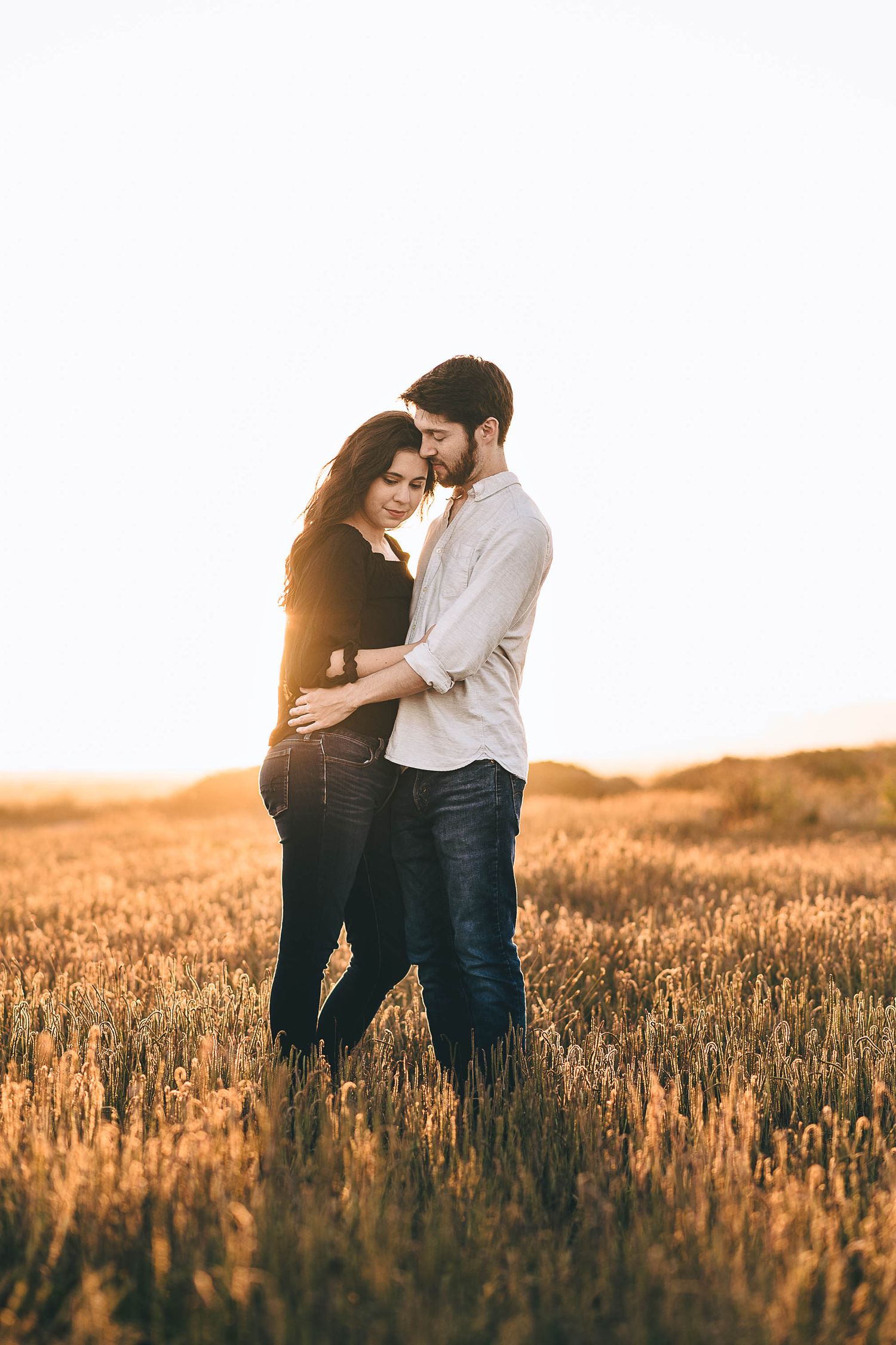 A couple embraces in a golden field during sunset creating a romantic silhouette.