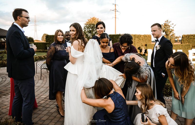 Wedding party gathered outdoors with guests adjusting the bride's dress.