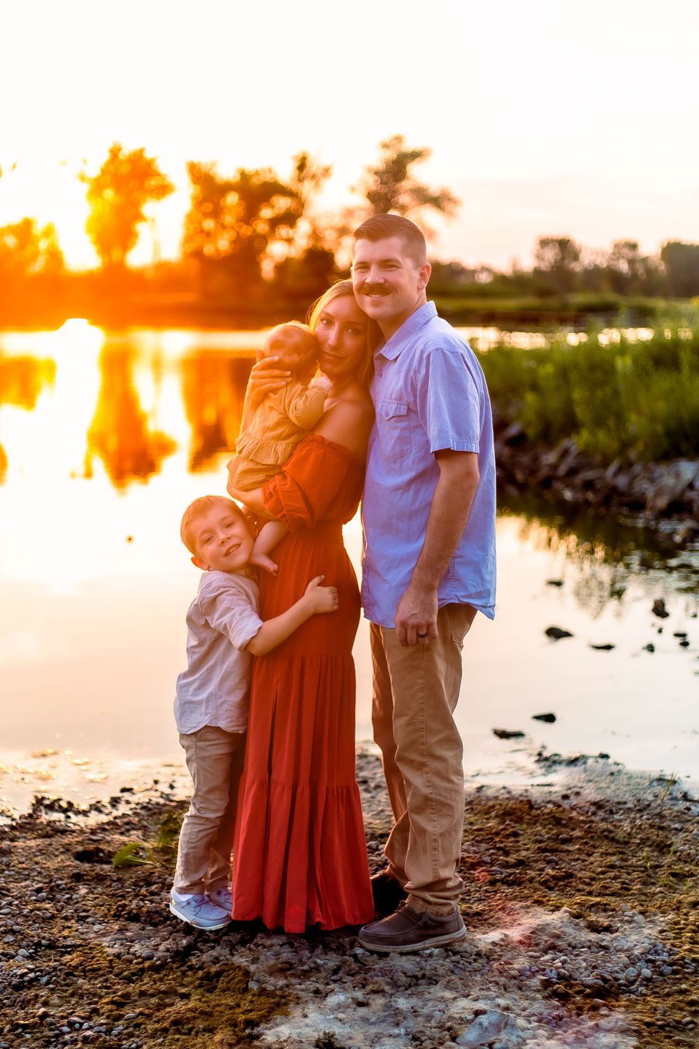 Family embracing during golden hour sunset by a reflective lake.