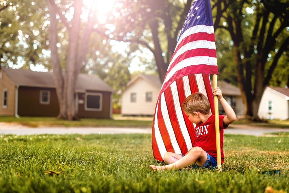 Child playing with American flag in sunny suburban yard.