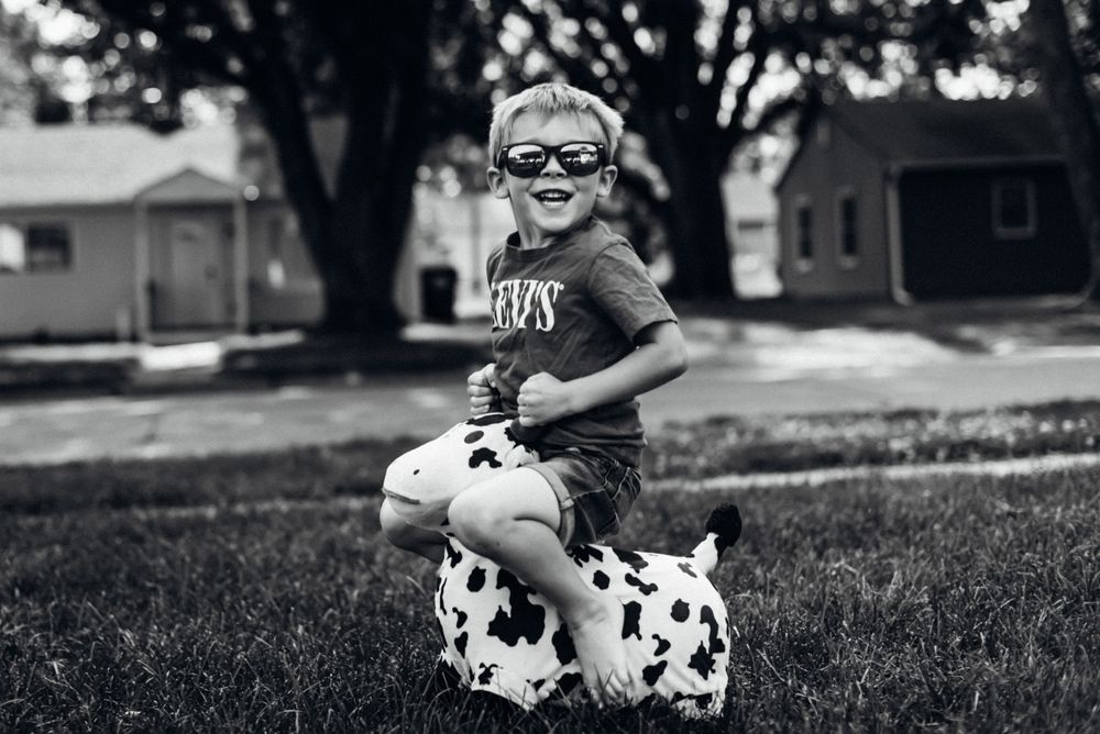 Child riding a spotted cow toy in a suburban yard.