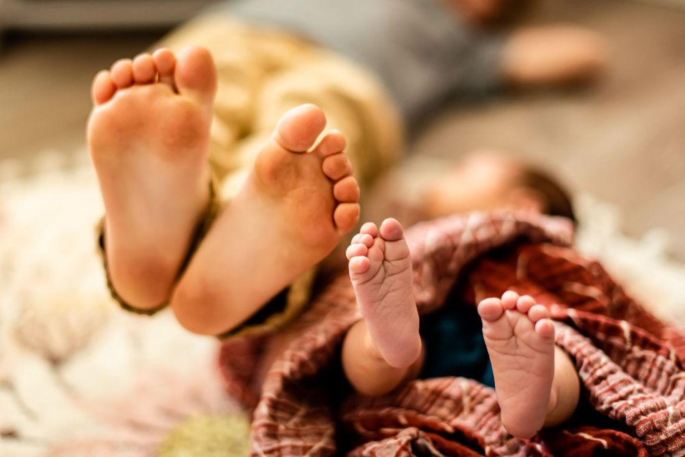 Close-up of baby and adult feet peeking out from under a cozy knit blanket.
