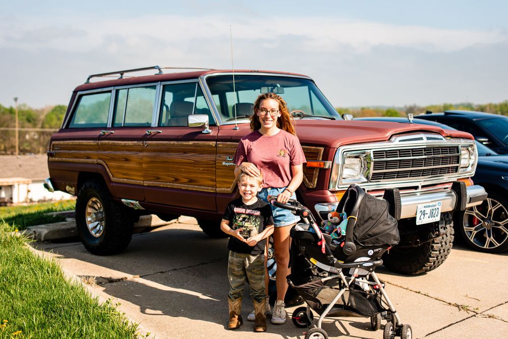Family posing with vintage wood-paneled SUV and stroller in parking lot.