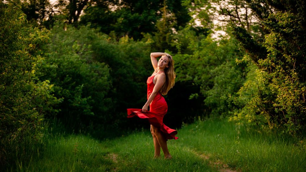 Woman in flowing red dress twirling in a sunlit green meadow.