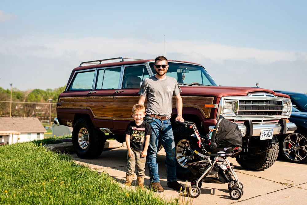Father and child standing beside classic brown wood-paneled SUV on sunny day.