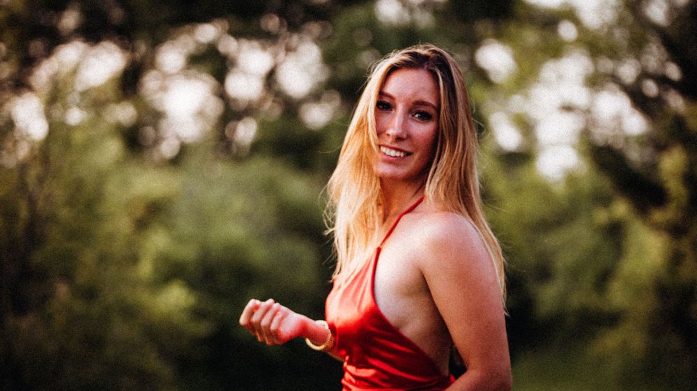A woman in a red outfit smiles during golden hour in an outdoor setting.