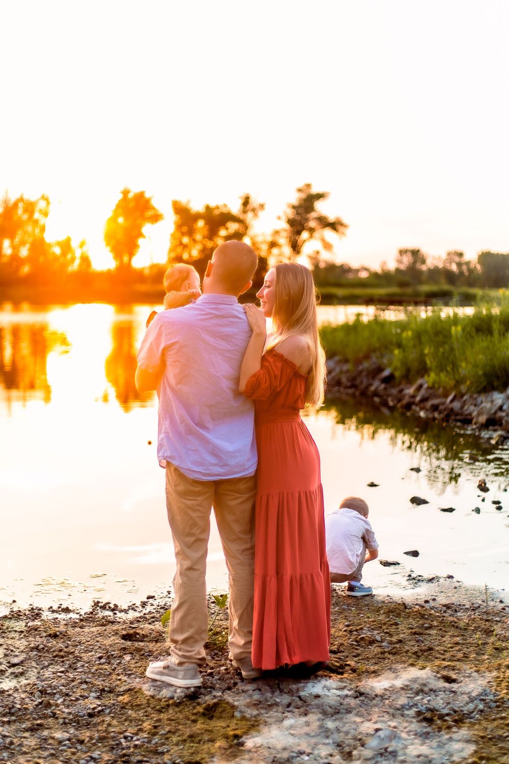 A couple stands by a lake at sunset, admiring the golden light reflecting off the water's surface.