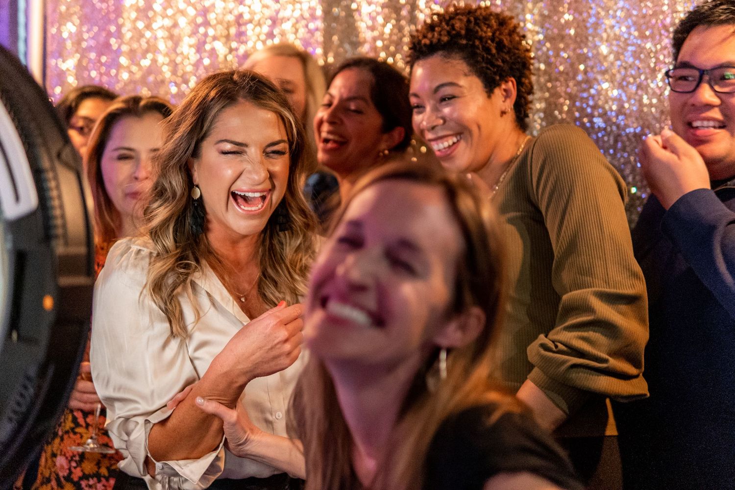 Group of friends laughing together at a sparkling party with festive lighting.