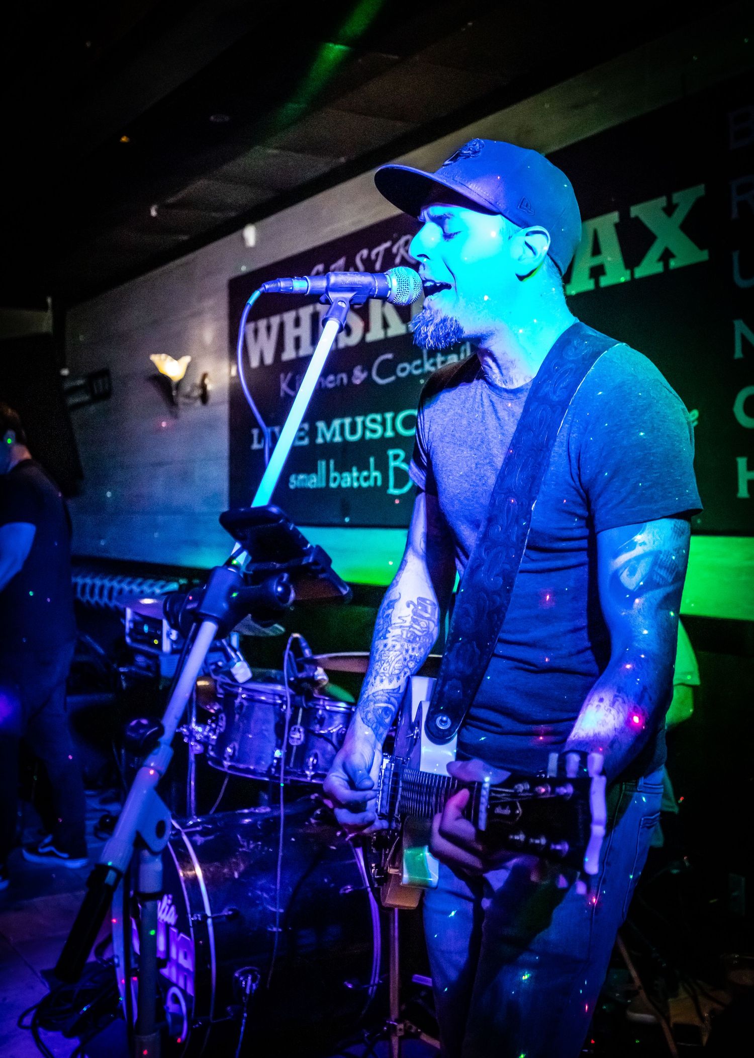 A performer plays guitar on stage bathed in blue lighting at a music venue.