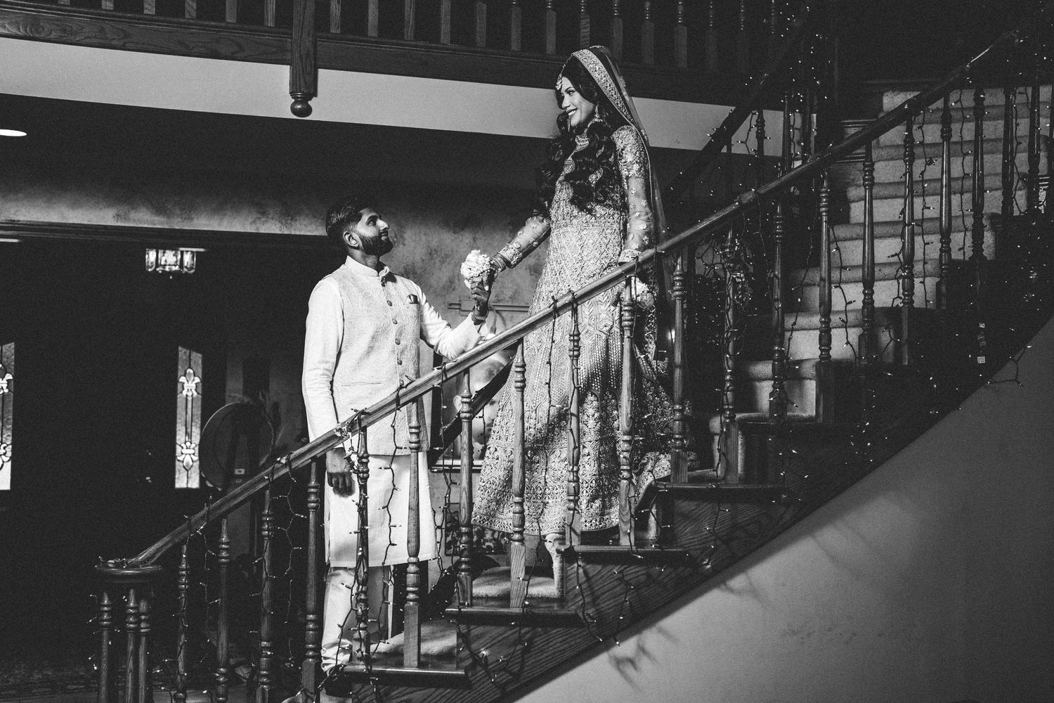 Newlyweds on winding stairs, a black and white tale. The man reaches up, gazes admiringly at his bride above